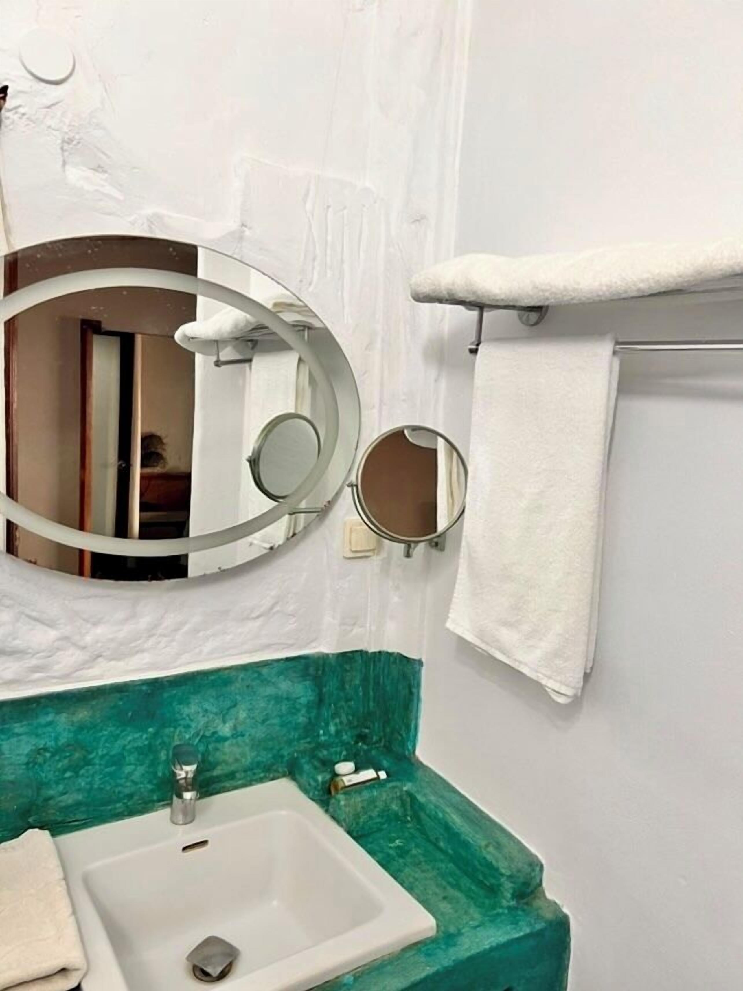 Ein Badezimmer mit einem weißen Waschbecken, zwei Spiegeln und einem Handtuchhalter.