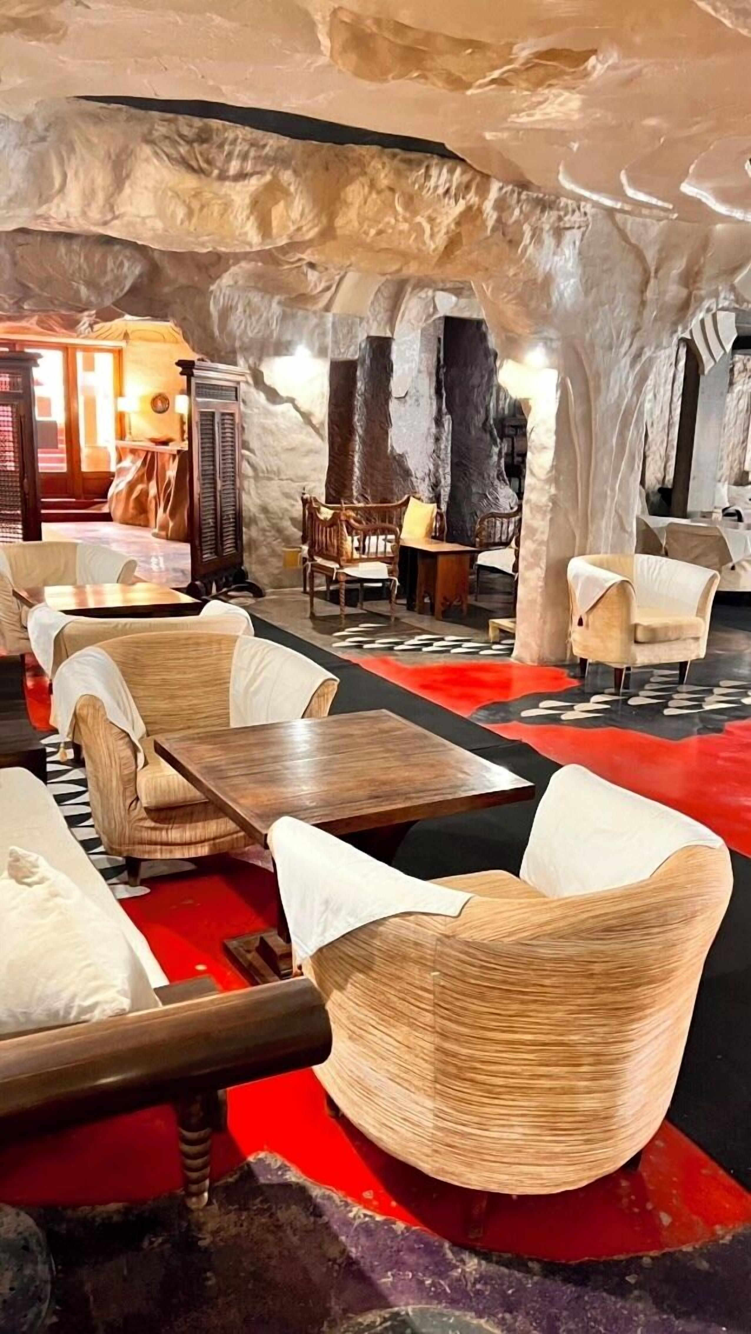 Un intérieur avec des tables et des chaises en bois, une moquette rouge et un mur qui ressemble à de la pierre.