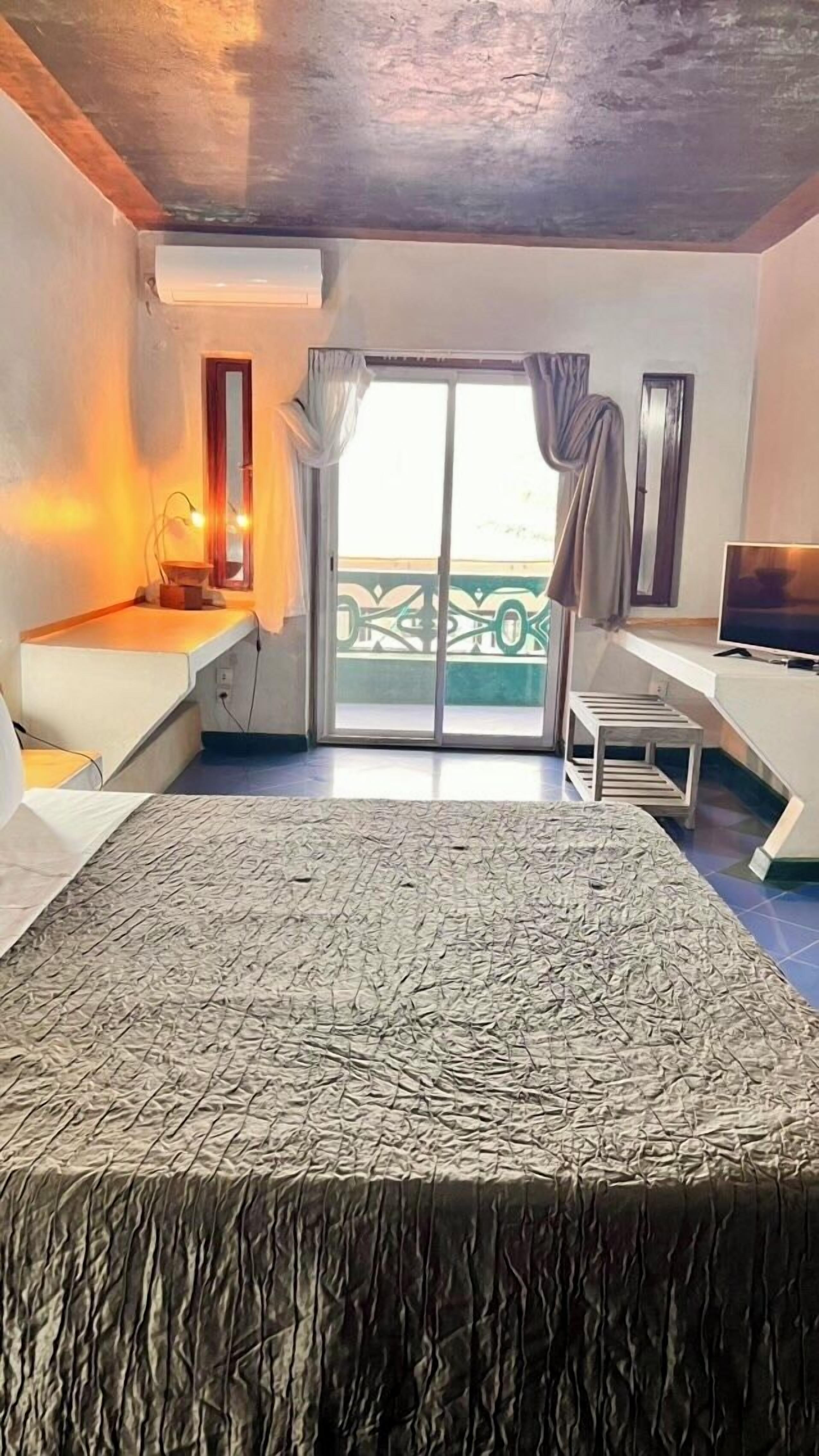 A hotel room with a bed, a desk, a chair, a TV, and a balcony with a view.