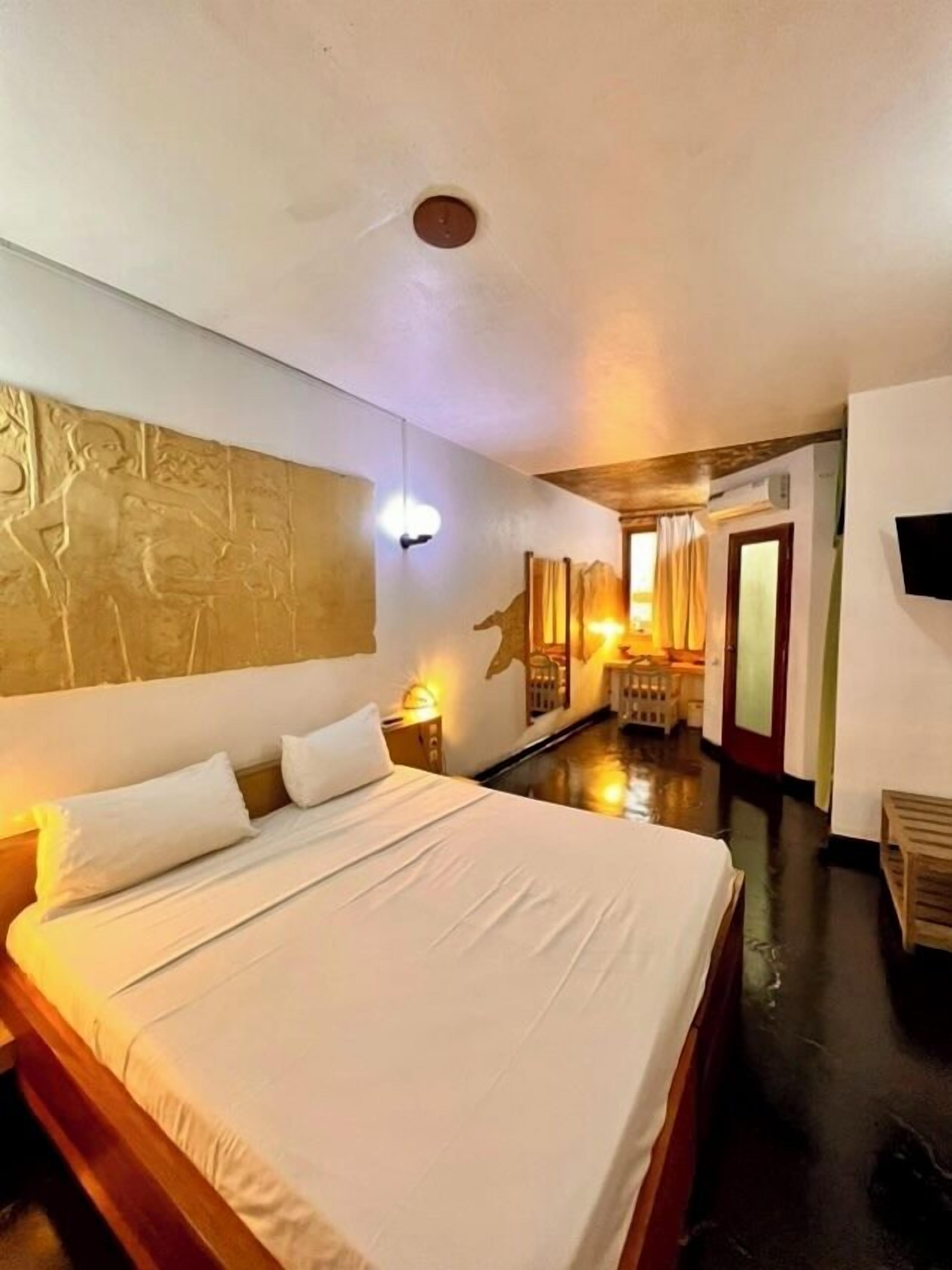 Una habitación de hotel con una cama grande, un televisor montado en la pared y un techo de madera.
