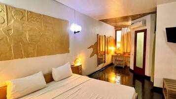 Une chambre d’hôtel avec un grand lit, un téléviseur fixé au mur et un plafond en bois.