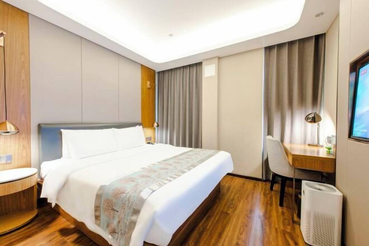 A hotel room with a bed, a desk, a chair, a TV, and a heater.