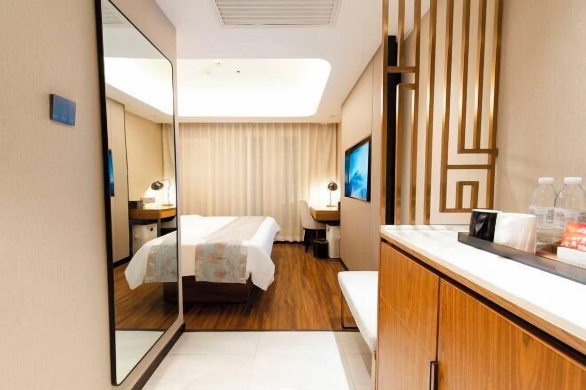 A hotel room with a bed, bedside table, mirror, and a desk with a chair.
