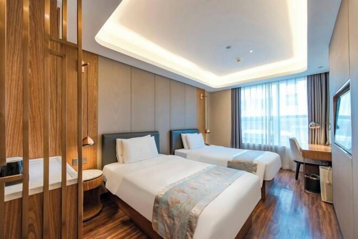 A modern hotel room with two beds, a desk, and a large window.