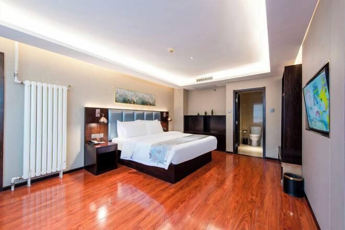 A modern hotel room with a large bed, a nightstand, a desk, and a bathroom visible through an open door.