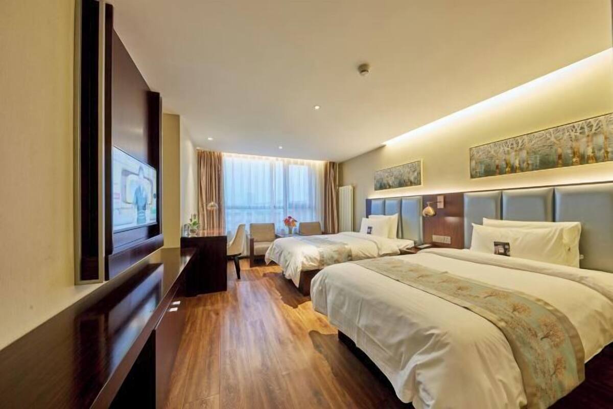 A hotel room with two beds, a desk, a chair, and a television.