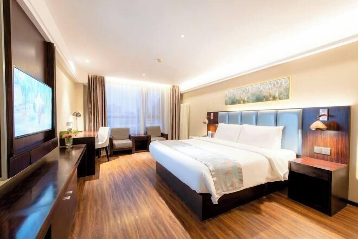 A hotel room with a large bed, a desk, a chair, a TV, and a window with curtains.