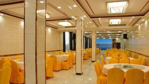 A banquet hall with round tables and yellow chairs, large windows, and a chandelier.