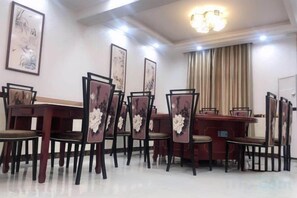A dining area with a long table and chairs, framed artwork on the walls, and a chandelier.