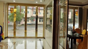 A hotel lobby with a glass door entrance, a seating area with a table and chairs, and a view of the outside.