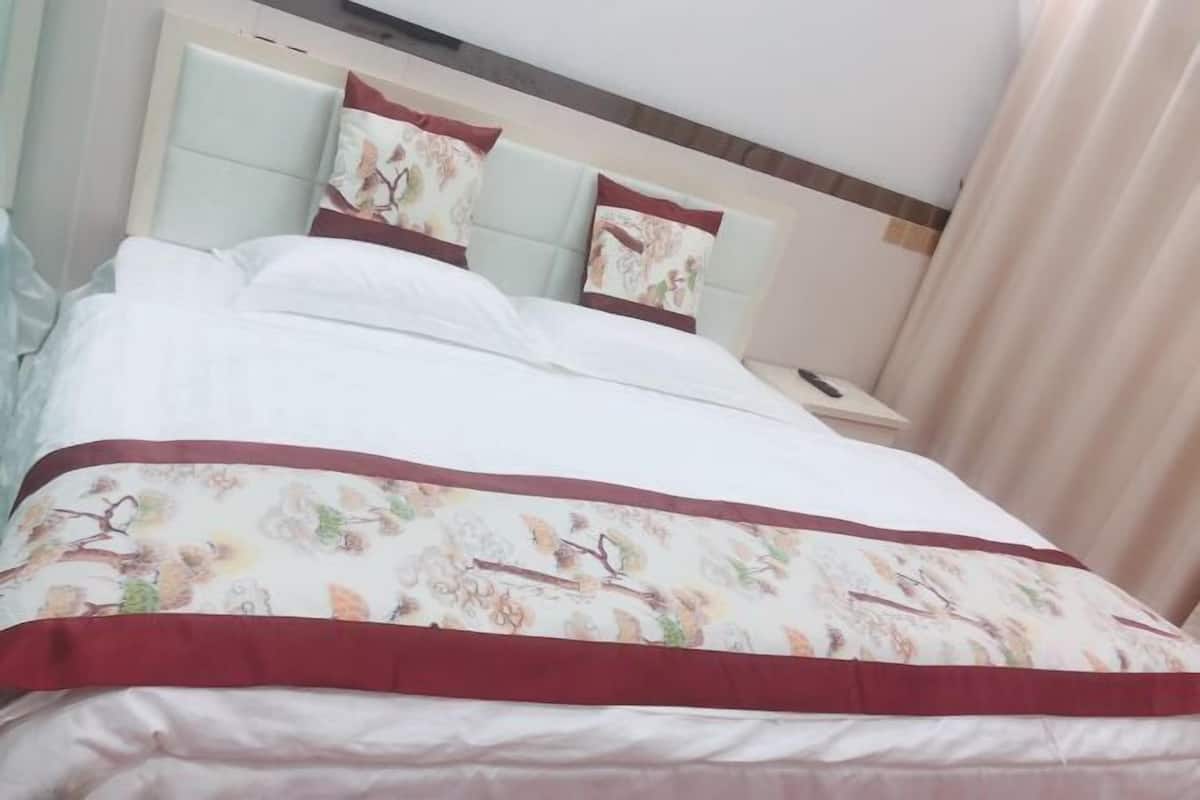 A neatly made bed with floral-patterned bedding and matching pillows, a headboard, and a bedside table.