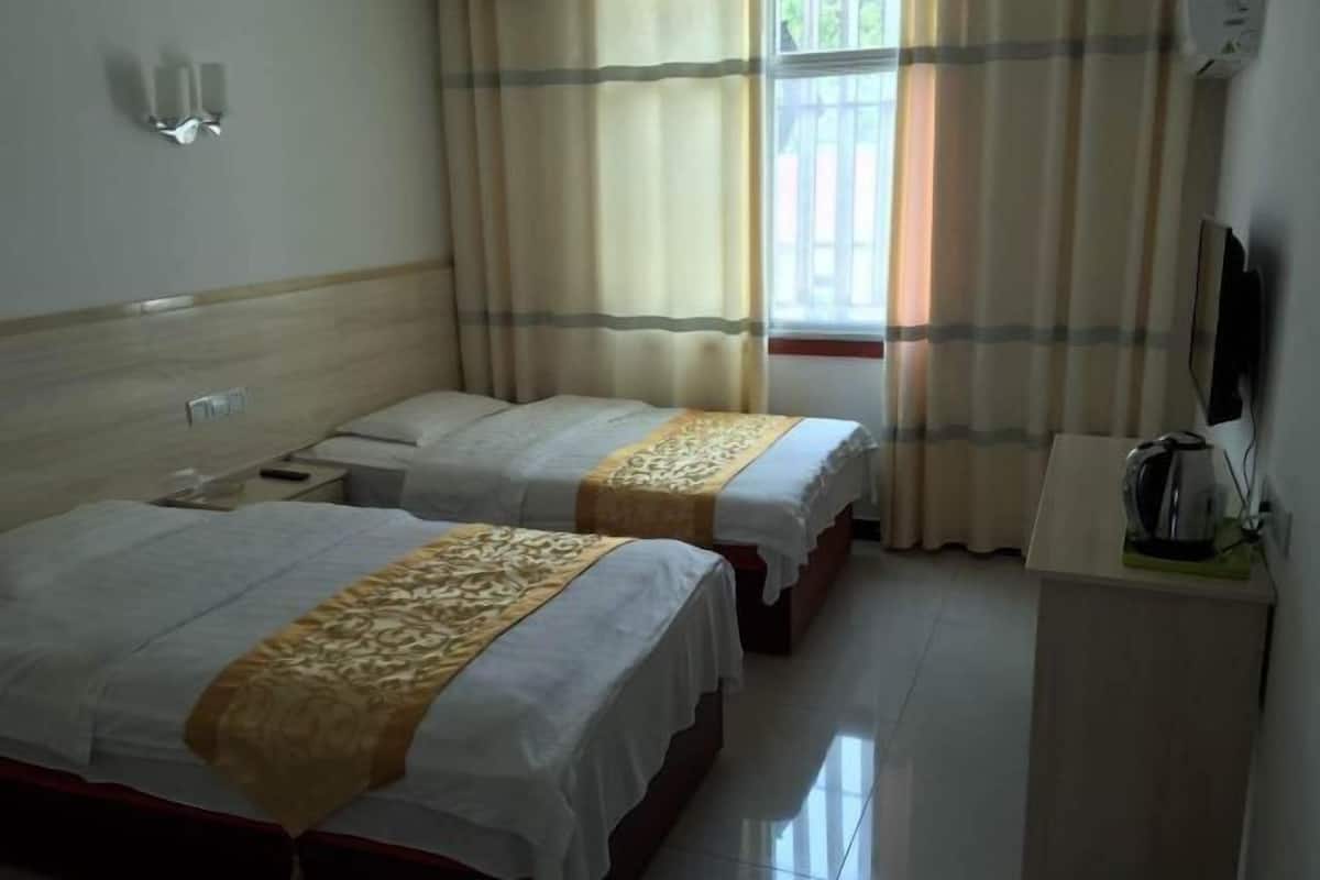 A hotel room with two beds, a television, a small desk, and a window with curtains.