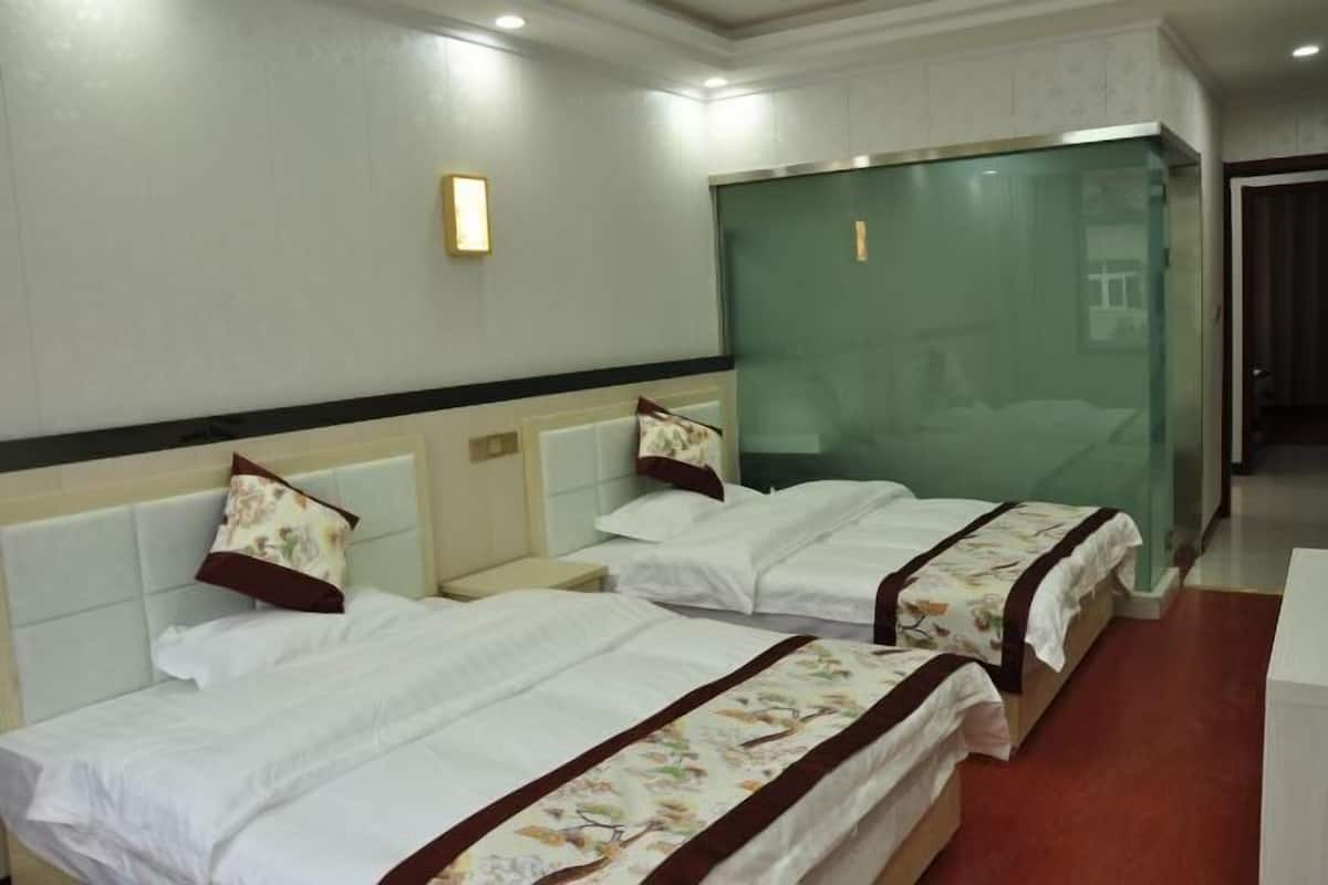 A hotel room with two beds, a nightstand, a bedside table, and a glass partition.
