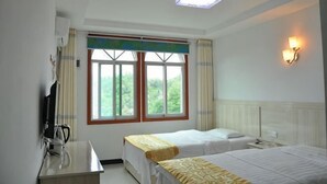 A hotel room with two beds, a desk, a TV, a window with curtains, and a wall-mounted light fixture.