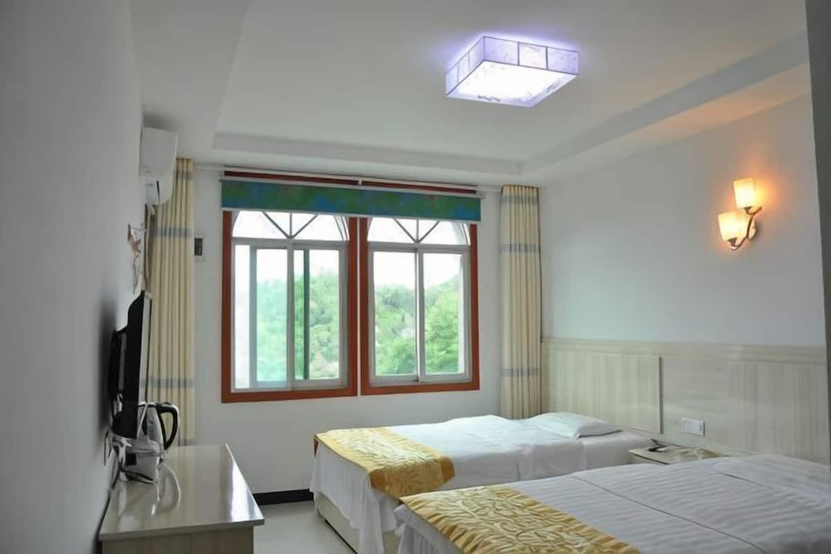 A hotel room with two beds, a desk, a TV, a window with curtains, and a wall-mounted light fixture.