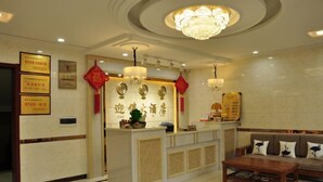A hotel reception area with a reception desk, a chandelier, and a sofa with decorative pillows.