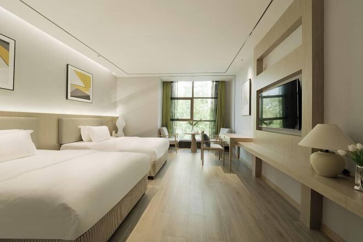 A hotel room with a large bed, a desk, a chair, a TV, and a window with curtains.