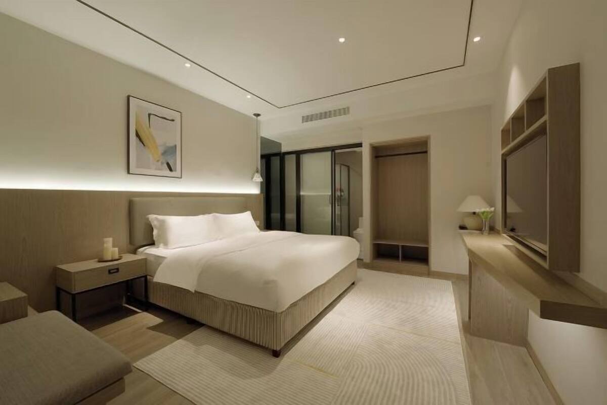 A modern bedroom with a large bed, bedside tables, a mirror, and a walk-in closet.