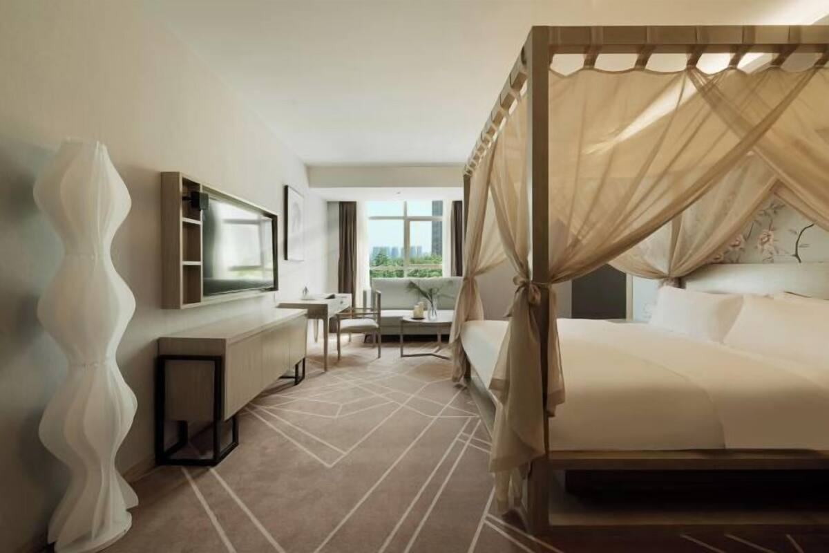 A modern hotel room with a large bed, a desk, and a view of the outdoors.