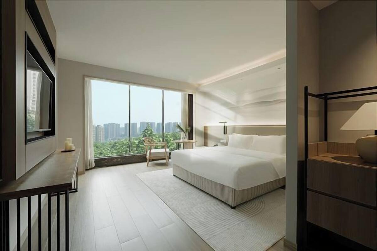 A modern bedroom with a large bed, a desk, and a view of a cityscape.