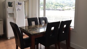 Un comedor con una mesa de mármol y cuatro sillas, un refrigerador blanco y una ventana con vistas a un área boscosa.