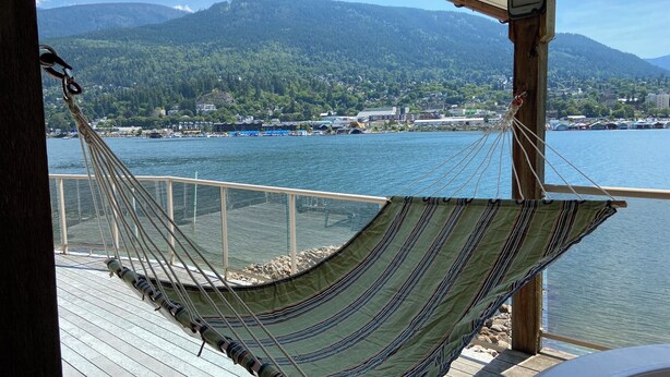 Una hamaca sobre una terraza de madera con vista a un cuerpo de agua y montañas al fondo.