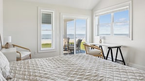 Une chambre avec un grand lit, un bureau et une chaise. Elle possède deux fenêtres donnant sur la plage.