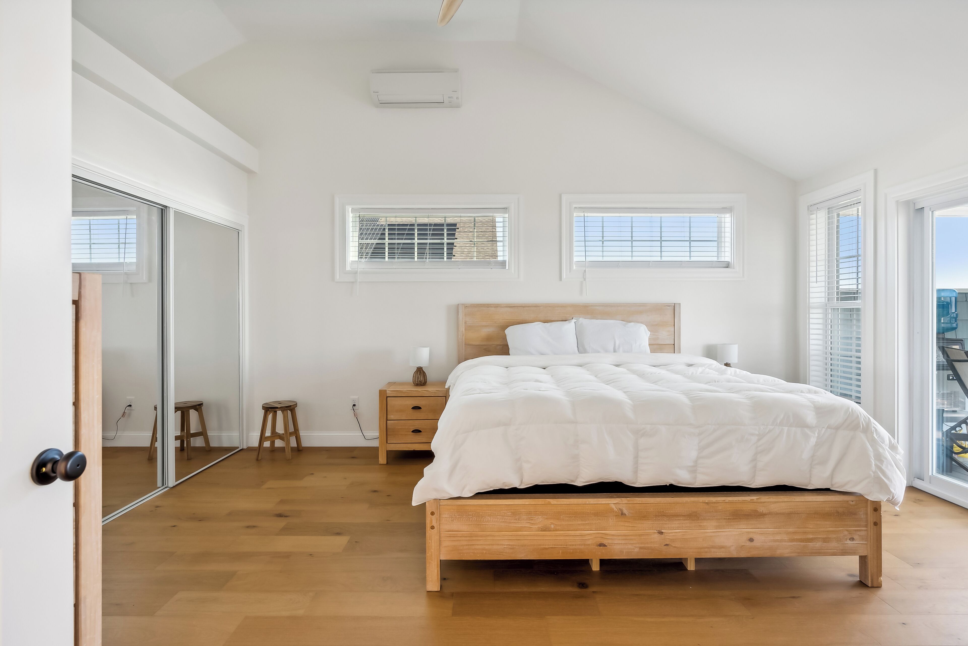 Une chambre à coucher avec un lit en bois, une table de chevet, un miroir et une fenêtre avec des stores.