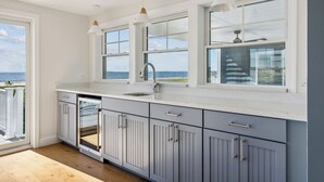 Une cuisine moderne dotée d’une grande fenêtre, de meubles blancs et offrant une vue sur l’océan.