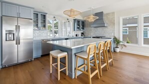 Une cuisine moderne dotée d’un grand îlot central, d’appareils électroménagers en acier inoxydable et de tabourets de bar en bois.