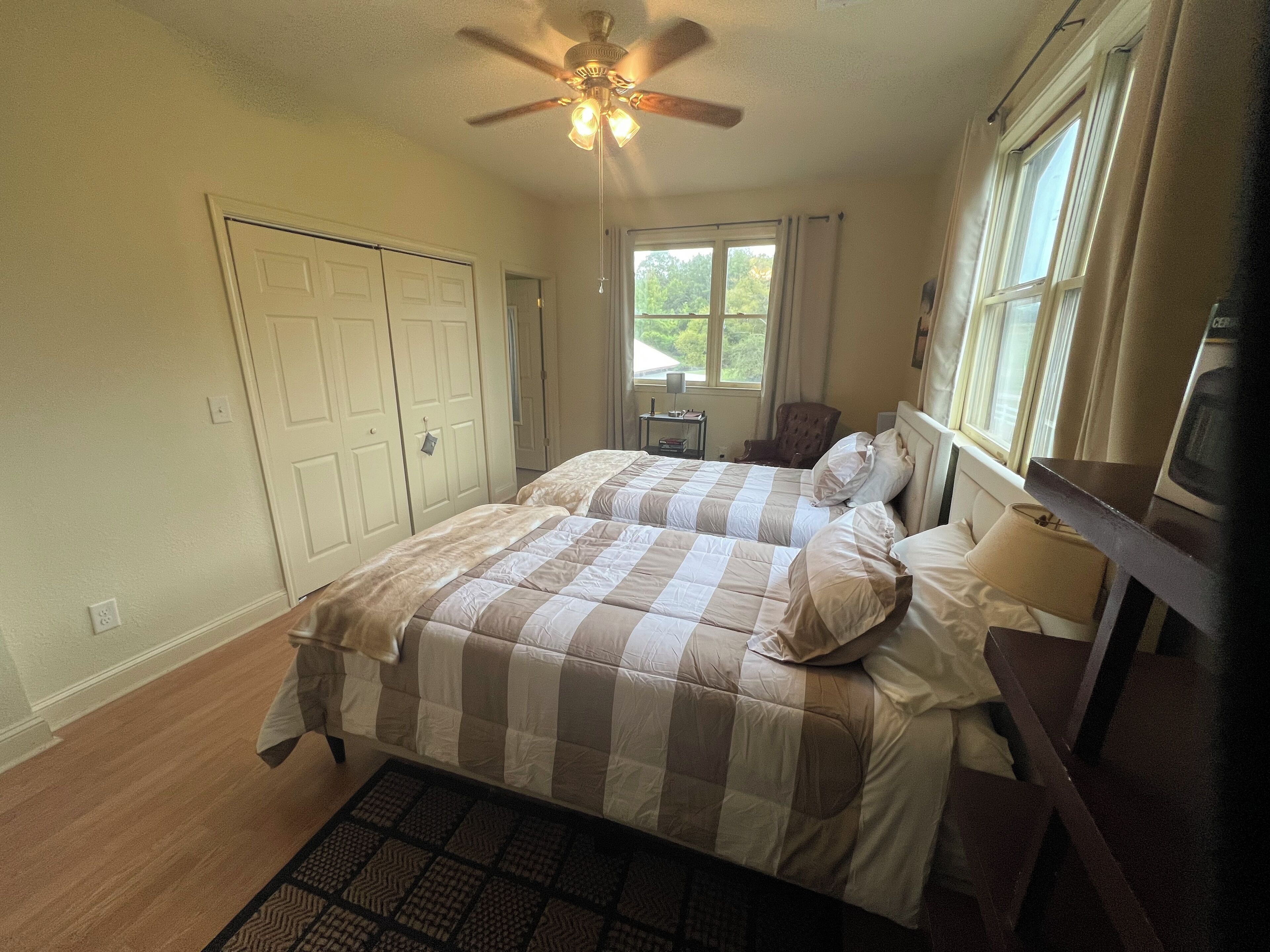 A bedroom with two beds, a ceiling fan, a window, a chair, and a nightstand.