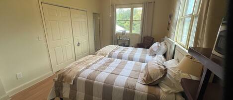 A bedroom with two beds, a ceiling fan, a window, a chair, and a nightstand.