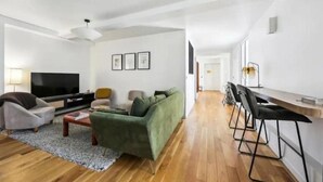 Una sala de estar moderna con un televisor de pantalla plana, un sofá verde, una mesa de centro y un comedor con una mesa larga y sillas.