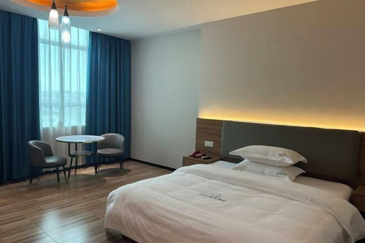 Habitación de hotel con cama, dos sillas, una mesita y ventana con cortinas.