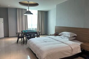 A hotel room with a bed, a desk with a chair, a table, and a hanging light fixture. - Yuanle Hotel (Boluo)