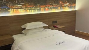 A hotel room with a bed, a nightstand, and a cityscape view through the window. - Yuanle Hotel (Boluo)