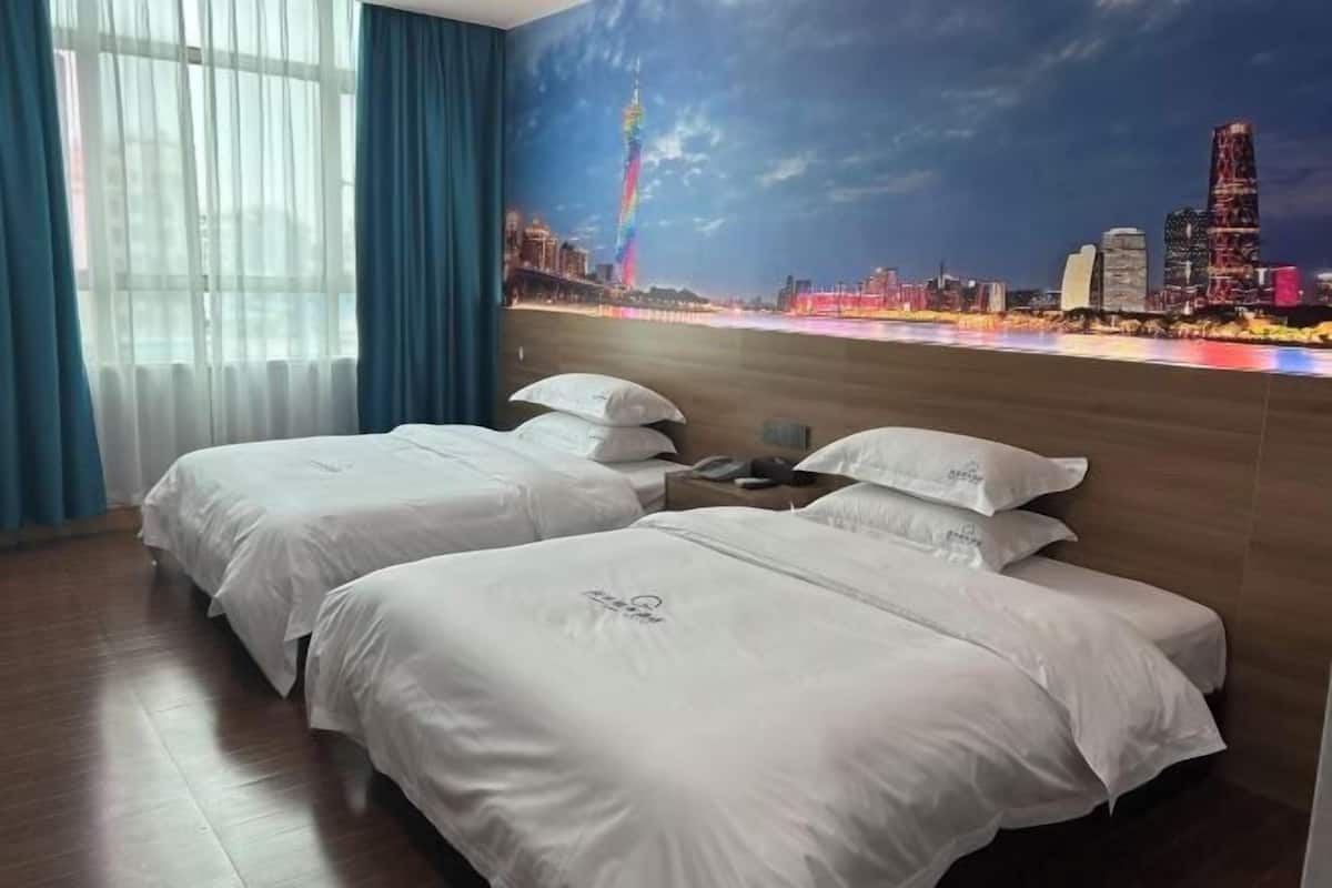 Habitación de hotel con dos camas, un mural de un paisaje urbano, suelo de madera y una ventana con cortinas.