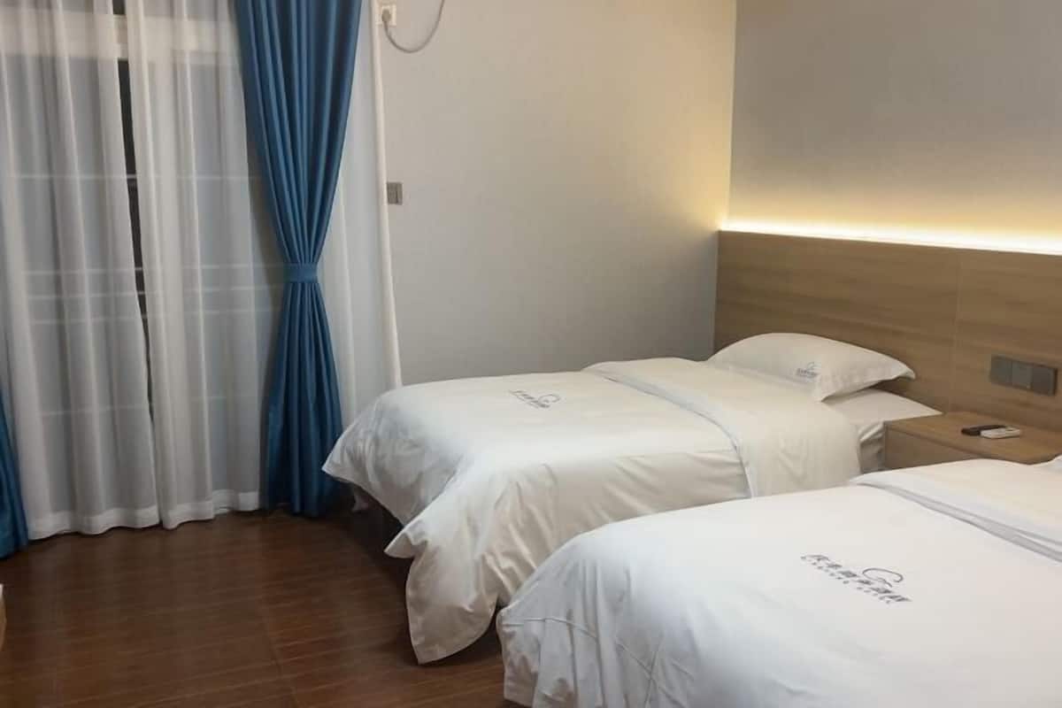 Habitación de hotel con dos camas, cabecera de madera, mesita de noche y lámpara de pared.