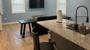 A modern kitchen with a granite countertop, a built-in sink, and a flat-screen TV mounted on the wall.