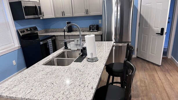 A kitchen with granite countertops, stainless steel appliances, and a wooden floor.
