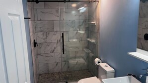 A bathroom with a glass-enclosed shower, a toilet, and a sink.