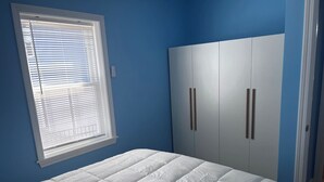 A bedroom with a bed, a window with blinds, and a wardrobe with two doors.