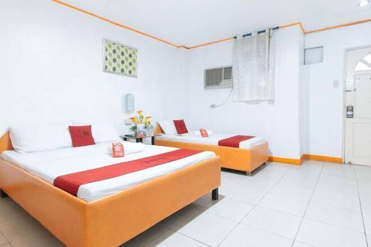 Quarto de hotel com duas camas, uma mesa pequena com um vaso e uma porta.