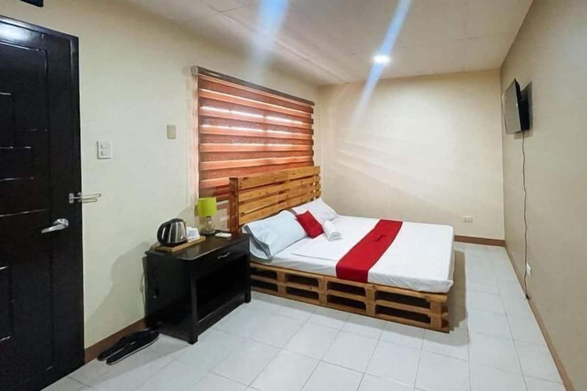 Quarto com cama, mesa de cabeceira, cabeceira de madeira, televisão fixada na parede e uma porta.
