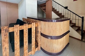 A reception desk with a wooden frame and a curved design, situated in a lobby with a staircase in the background.