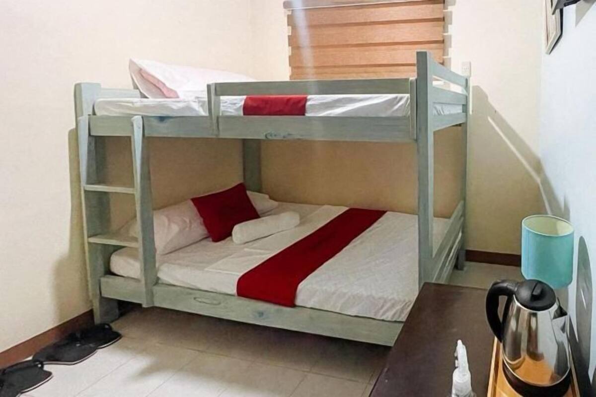 Uma cama beliche com colcha vermelha e branca, uma escada de madeira e uma chaleira sobre um tabuleiro.