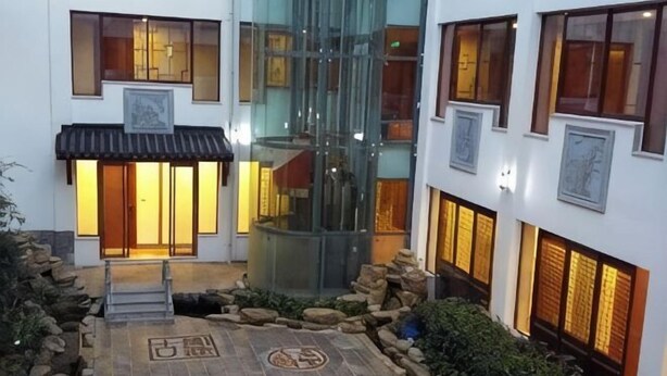 A traditional building with a courtyard, stone pathway, and a glass elevator. - Shanghecheng Hotel (Feixi)