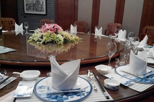 Mesa de conferência com arranjo floral, guardanapos brancos e pratos azul e branco.