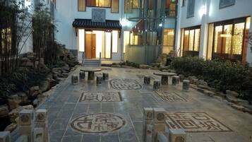 A courtyard with stone benches, a tiled floor with traditional patterns, and a building entrance with a glass door.