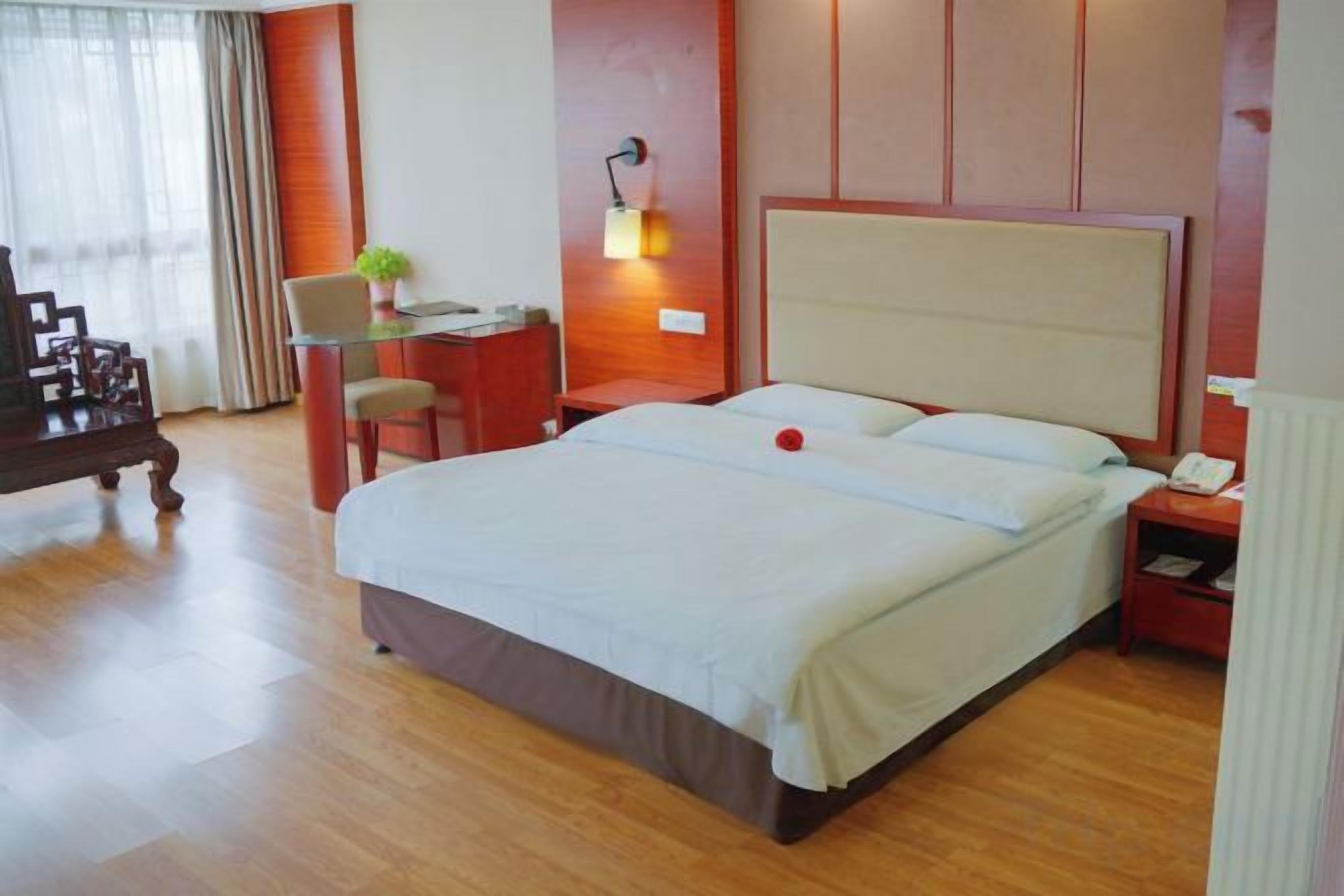 A hotel room with a bed, desk, chair, lamp, and a small table with a plant.